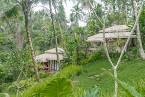 A bungalow with a thatched roof, surrounded by lush greenery and palm trees. - Galalima Glamping (Selemadeg)