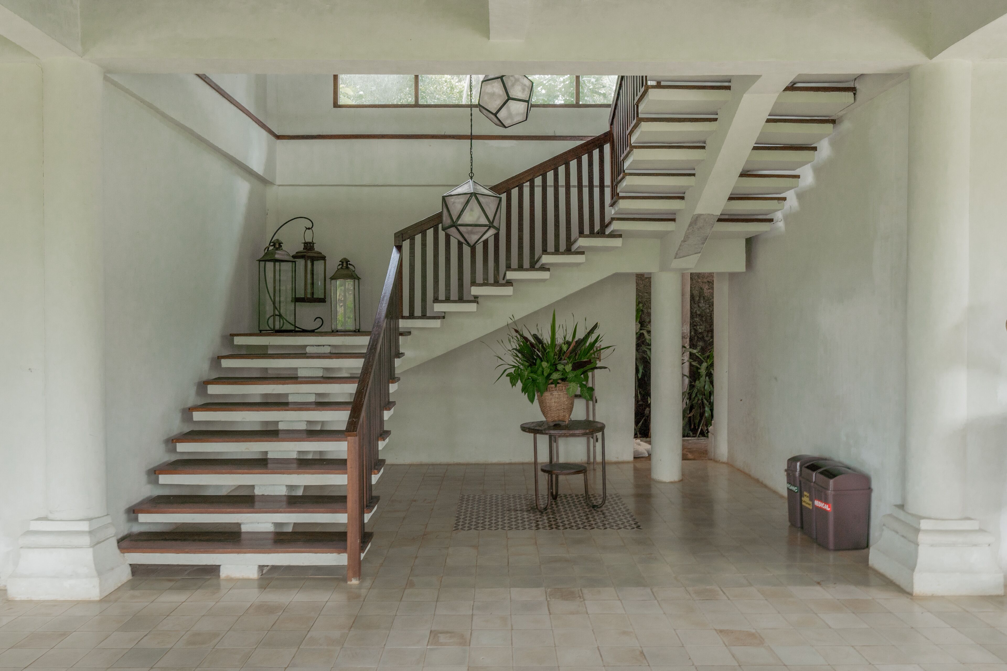A spacious interior with a staircase, a potted plant, and a trash bin.