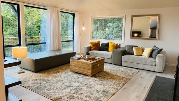 Una sala de estar moderna con un conjunto de sofá, una mesa de centro y ventanas amplias con vista a la vegetación.