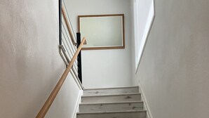 Una escalera de madera con barandilla, que lleva a un rellano con un espejo enmarco.