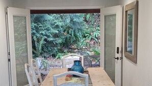Un comedor con una mesa y sillas de madera, un tapete y vistas a un jardín a través de puertas de vidrio.