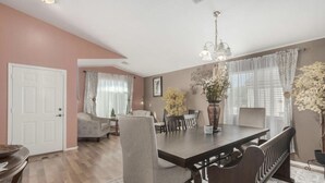 A dining area with a large table, chairs, and a chandelier. There is a door and a window with curtains. - Pet-Friendly and Family-Friendly (Casa Grande)