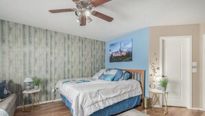 A bedroom with a bed, a ceiling fan, a nightstand, a wall-mounted clock, and a door. - Pet-Friendly and Family-Friendly (Casa Grande)