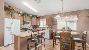 A modern kitchen with wooden cabinets, a central island with bar stools, a dining area with a round table and chairs, and decorative plants on the cabinets. - Pet-Friendly and Family-Friendly (Casa Grande)