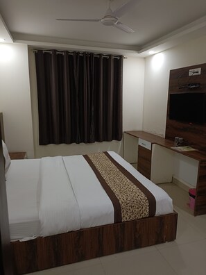 A bedroom with a bed, a desk, a television, and a ceiling fan. - Dalton Hotels  (New Delhi)