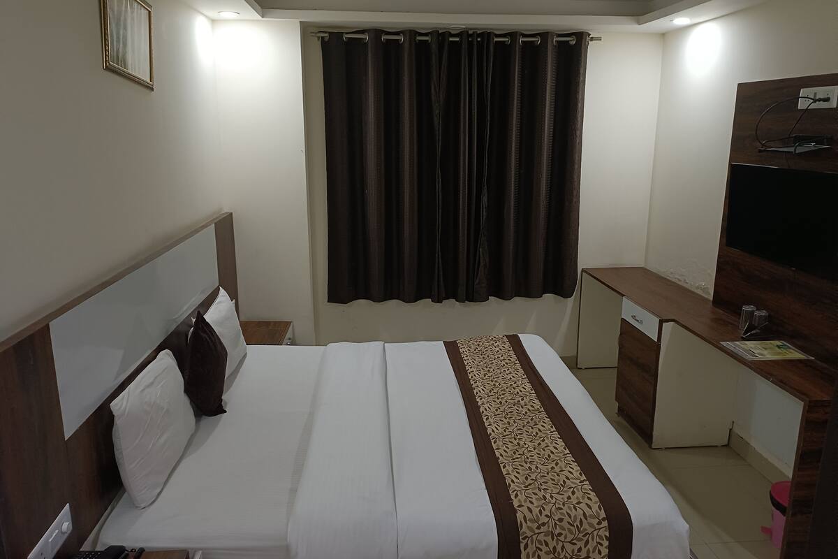 A hotel room with a bed, desk, television, and curtains.