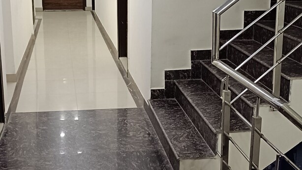 A modern hallway with a marble floor, a wooden door at the end, and a staircase with metal railings. - Dalton Hotels  (New Delhi)