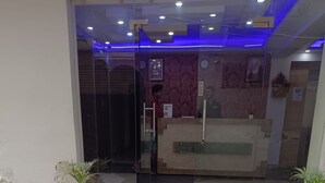 A hotel entrance with a reception desk, a glass door, and steps leading up to the entrance. There are two potted plants on either side of the steps. - Dalton Hotels  (New Delhi)