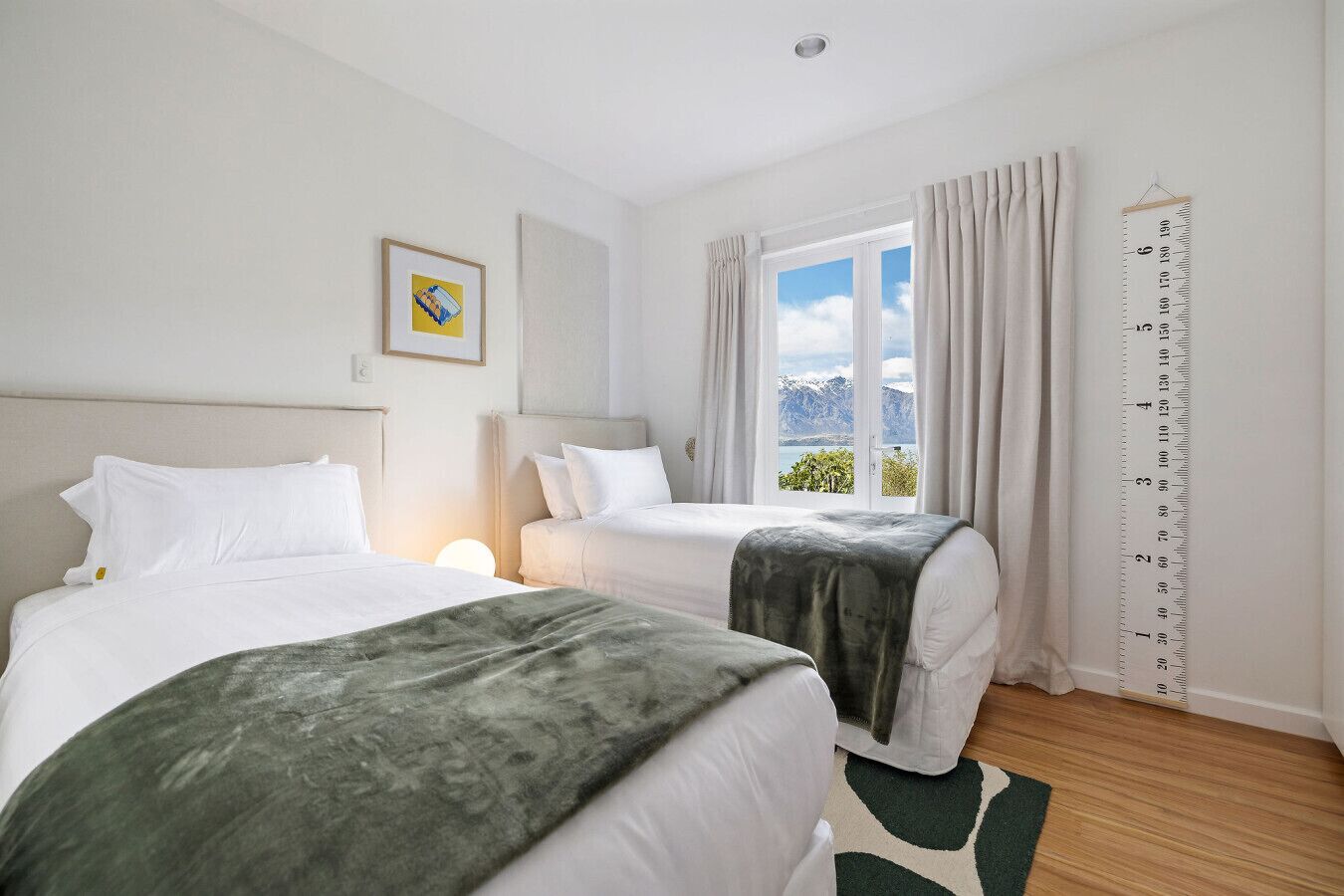 A hotel room with two beds, a large window with a mountain view, and a curtain rod with a height chart.