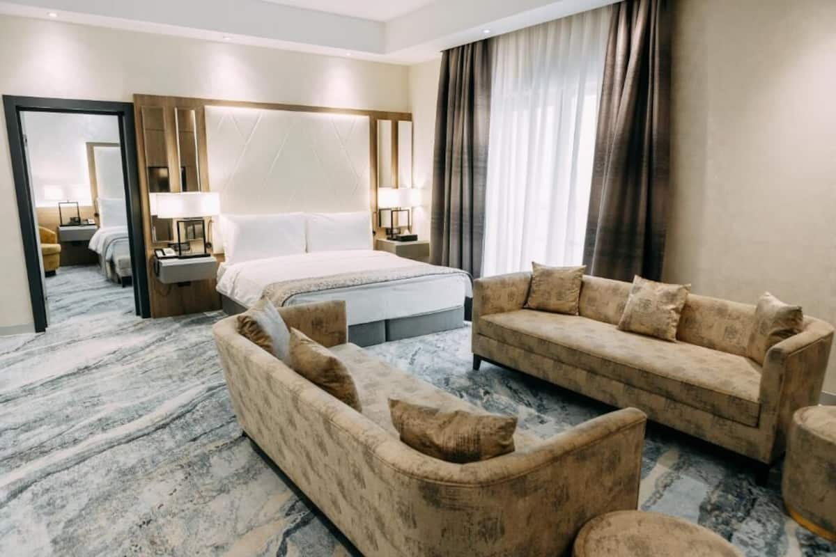 A hotel room with a large bed, a sofa, a chair, and a desk with a lamp.