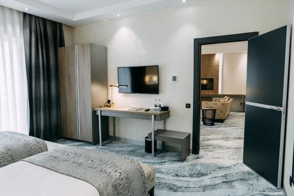 A modern hotel room with a bed, a desk with a flat-screen TV, a small table, and a sofa.