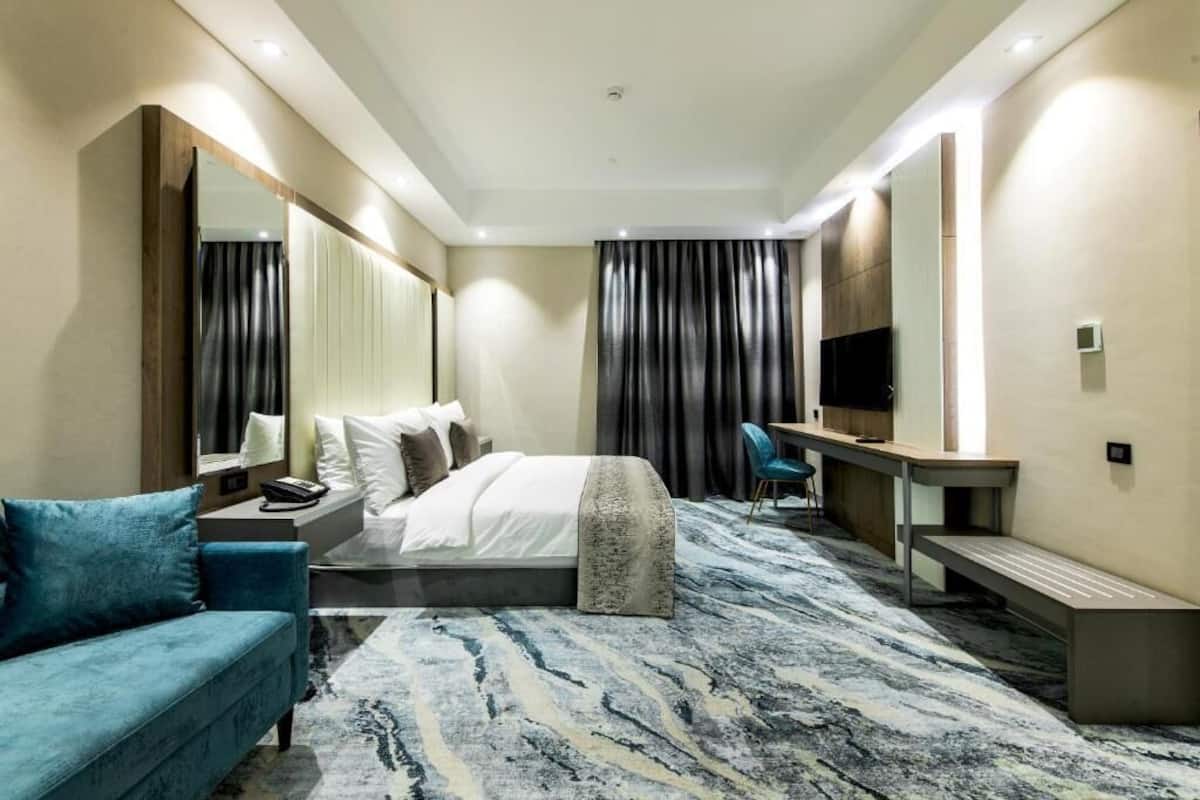 A modern hotel room with a bed, a sofa, a desk, a chair, and a large mirror.