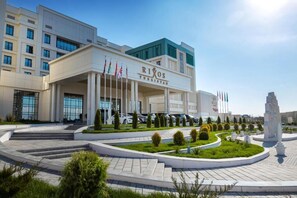 A modern hotel with a central entrance, multiple flags, and a landscaped garden area.