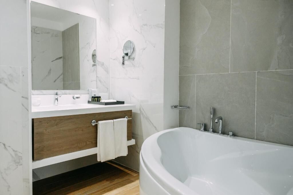 Une salle de bain moderne avec une grande baignoire, un meuble-lavabo en bois, un miroir et des carreaux de marbre.