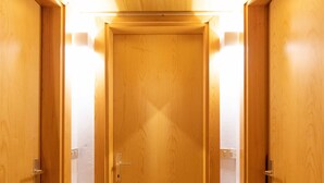 Een houten gang met een deur aan het einde, verlichting op de muren en een vloerbedekking.