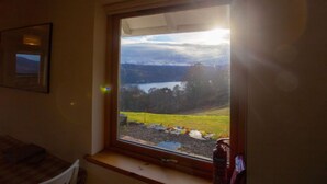 A room with a large window overlooking a landscape with a lake and mountains.