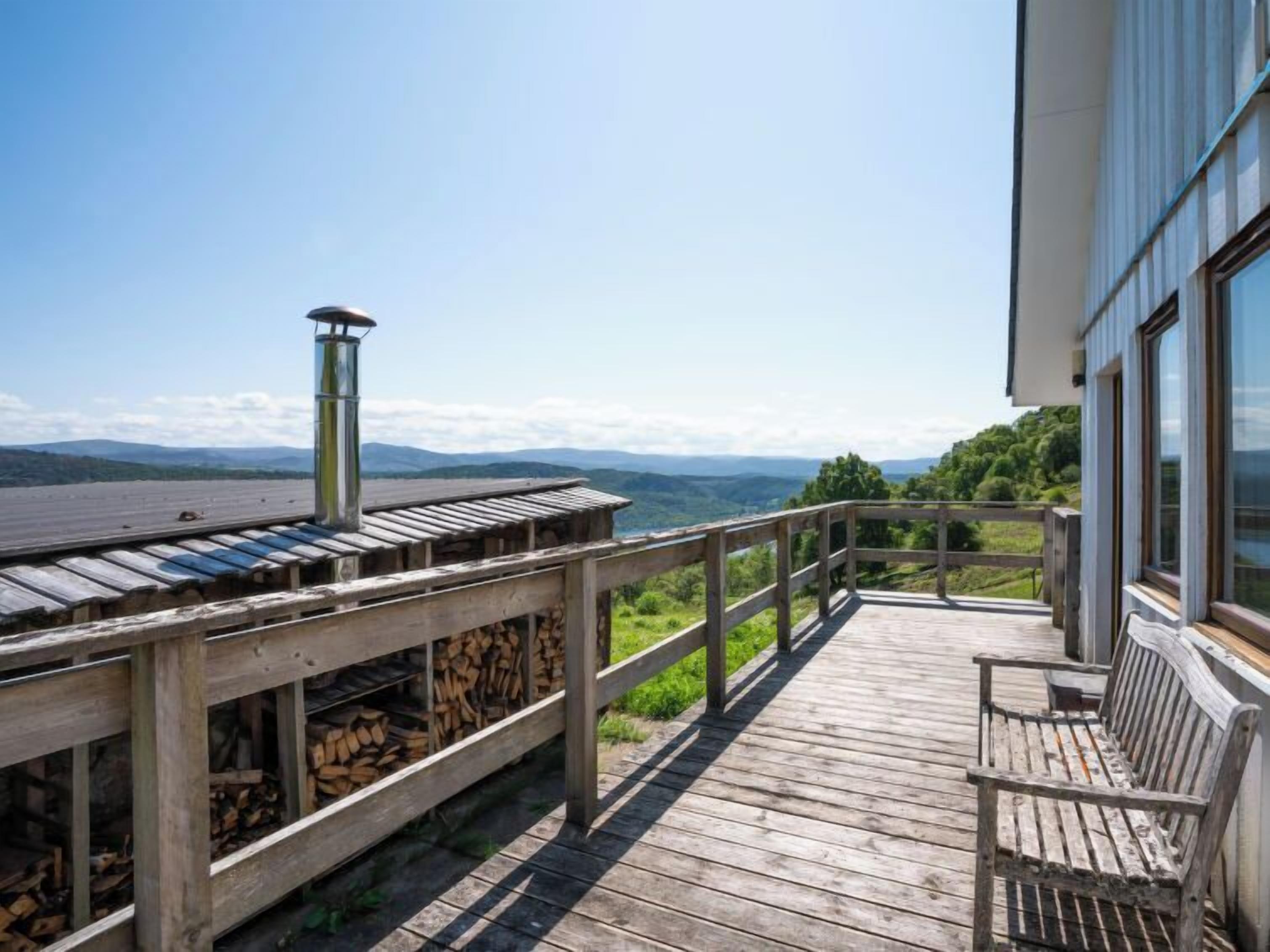 A wooden deck with a railing, a stack of firewood, and a view of mountains.