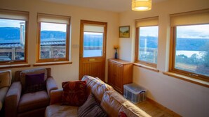 A cozy living room with a sofa, a wooden cabinet, and a view of mountains through large windows.
