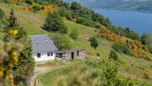 A house with a sloped roof, a stone extension, and a view of a lake.