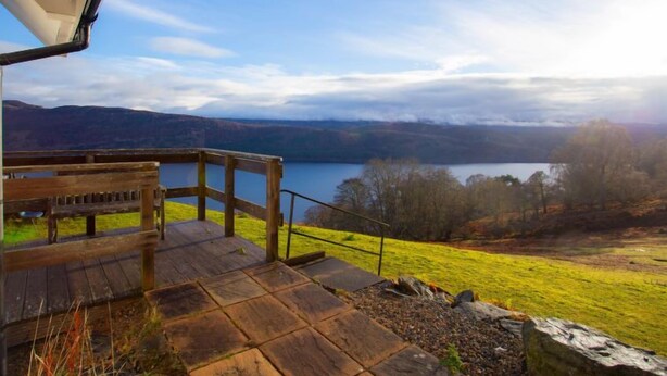 A wooden deck with a bench overlooking a lake and hills.
