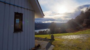 A white building with a window and a view of a lake and hills in the background.