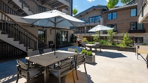 Een terras met een eettafel en stoelen, omringd door plantenpotten en parasols.