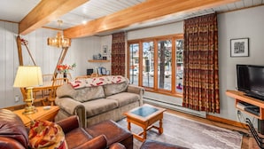 Een gezellige woonkamer met een houten plafond, een bank, een salontafel en een televisie.