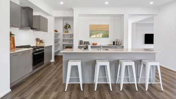 A modern kitchen with a central island, bar stools, a stove, and a built-in oven. - City & Surf Getaway - Luxe, Spacious, Sleeps 12 (Armstrong Creek)