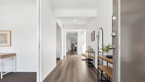 A hallway with wooden flooring, white walls, and a bench with a potted plant. - City & Surf Getaway - Luxe, Spacious, Sleeps 12 (Armstrong Creek)