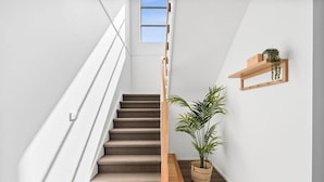 A modern staircase with a wooden handrail, a potted plant, and a wooden shelf with a plant. - City & Surf Getaway - Luxe, Spacious, Sleeps 12 (Armstrong Creek)