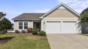 A single-story house with a garage, a front door, and a small front yard with a lawn and some shrubs.