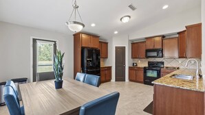 A modern kitchen with wooden cabinets, a granite countertop, and a dining area with a wooden table and blue chairs. - Peaceful Midland Cottage- Family & Pet Friendly, Near Golf, Parks, Nature Trail & Shopping! +15% Off (Midland)
