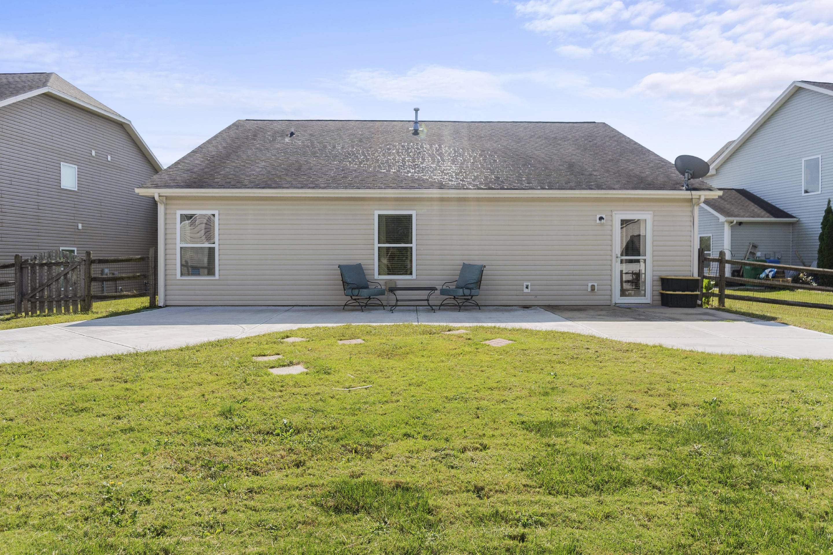 A single-story house with a covered patio, two chairs, and a small table.