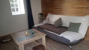 A cozy room with a wooden floor, a white sofa with cushions, a small wooden table, and a brown ottoman. - Gîte "des coussieres" between peace and nature (Courteix)