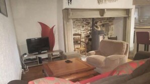 A living room with a sofa, a TV, a fireplace, and a stone wall. - Gîte "des coussieres" between peace and nature (Courteix)