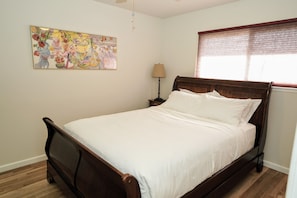 Un dormitorio con cama de madera, una mesita de noche, una lámpara y un ventanal con persianas.