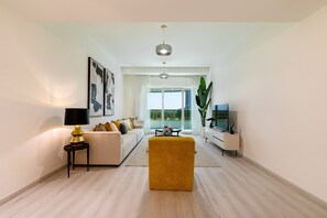 Un salon moderne avec un canapé, un pouf jaune, un téléviseur et une grande fenêtre.