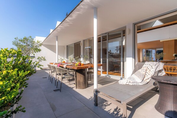 A modern outdoor patio with a dining table, chairs, and a lounge area.