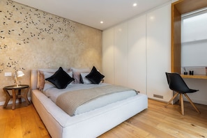 Ein modernes Schlafzimmer mit einem großen Bett, einem Nachttisch mit Lampe, einem Sessel und einer Wand mit einem Blattmuster.