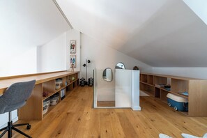 A modern, open-plan living space with a wooden floor, a desk, a chair, and shelves with various items.