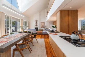 Une cuisine moderne dotée d’un îlot central, de planchers en bois et d’un coin repas avec une longue table et des chaises.