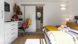 Une chambre d’hôtel avec un lit, un bureau et une chaise, un miroir et une salle de bain visible à travers une porte ouverte.