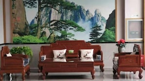 Ein traditionelles Holzsofa mit passenden Sesseln und einem Beistelltisch, vor einem großen Landschaftsbild platziert.
