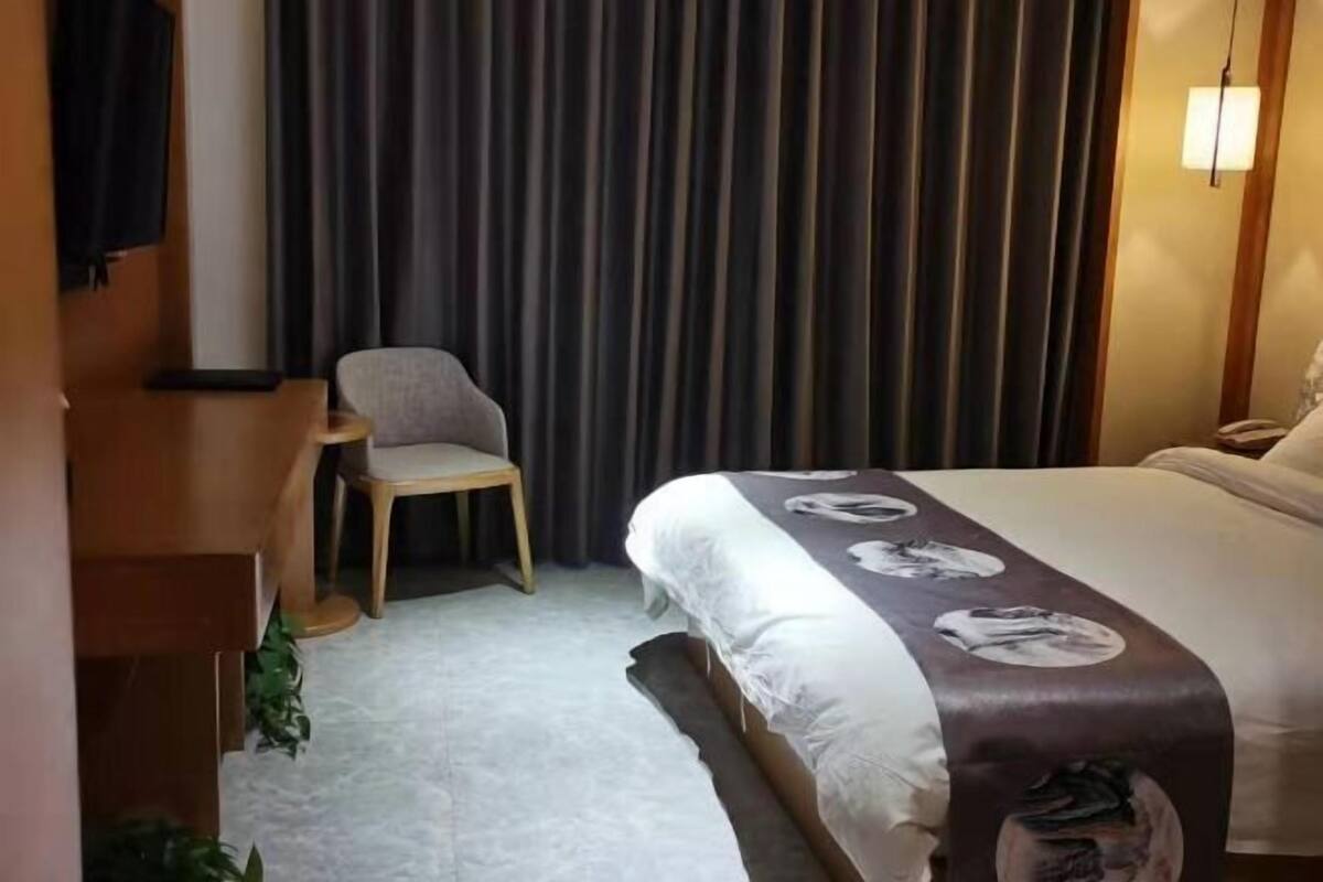 A hotel room with a bed, a chair, a desk, and a curtain.