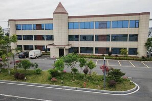 A multi-story building with a central tower, parking lot, and landscaped area with trees and shrubs. - Wanshun Hotel (Yangtai Airport) (Yangzhou)