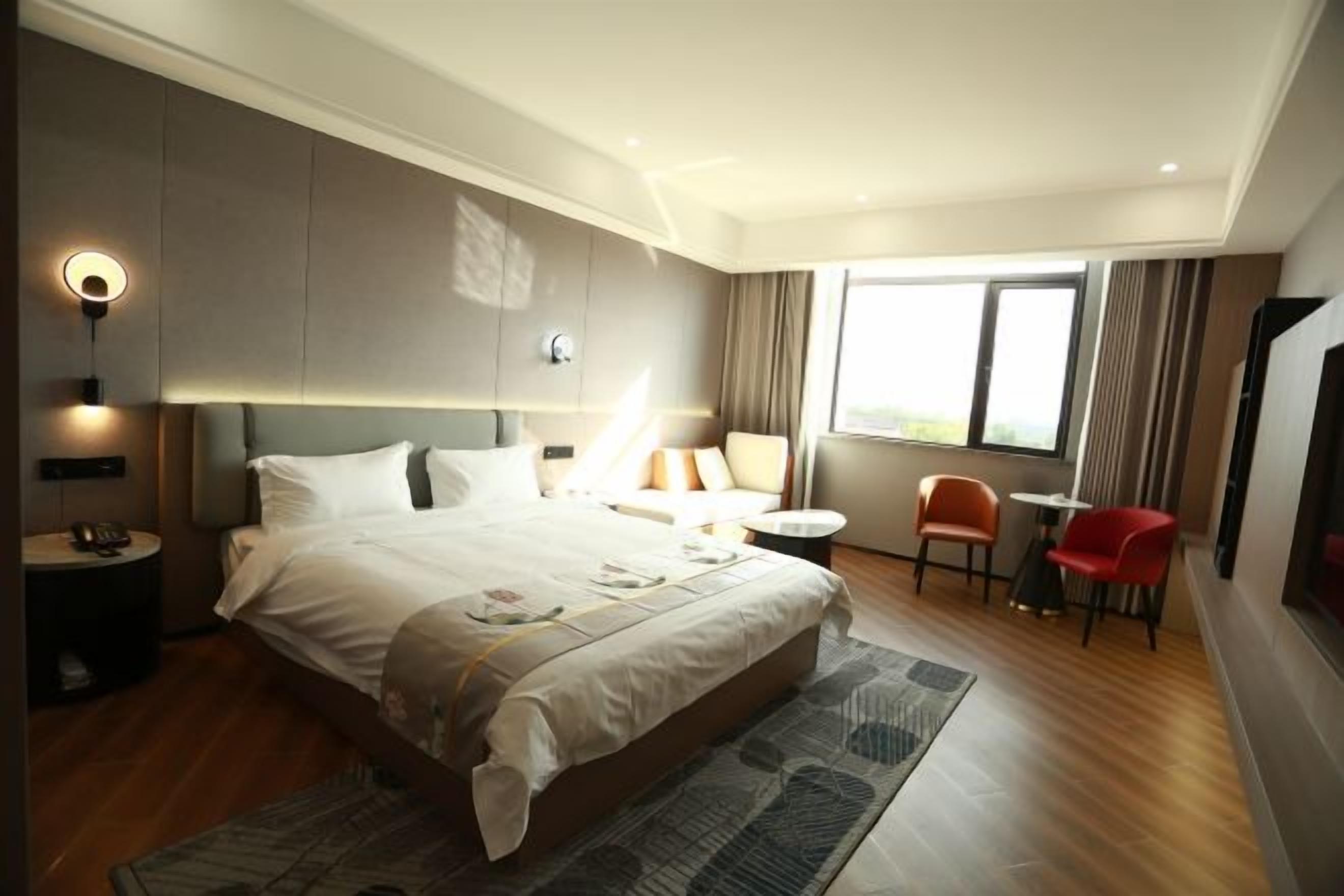 A modern hotel room with a large bed, a small round table, two chairs, a desk, and a large window.