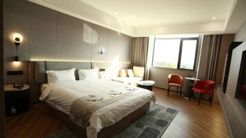 A modern hotel room with a large bed, a small round table, two chairs, a desk, and a large window.