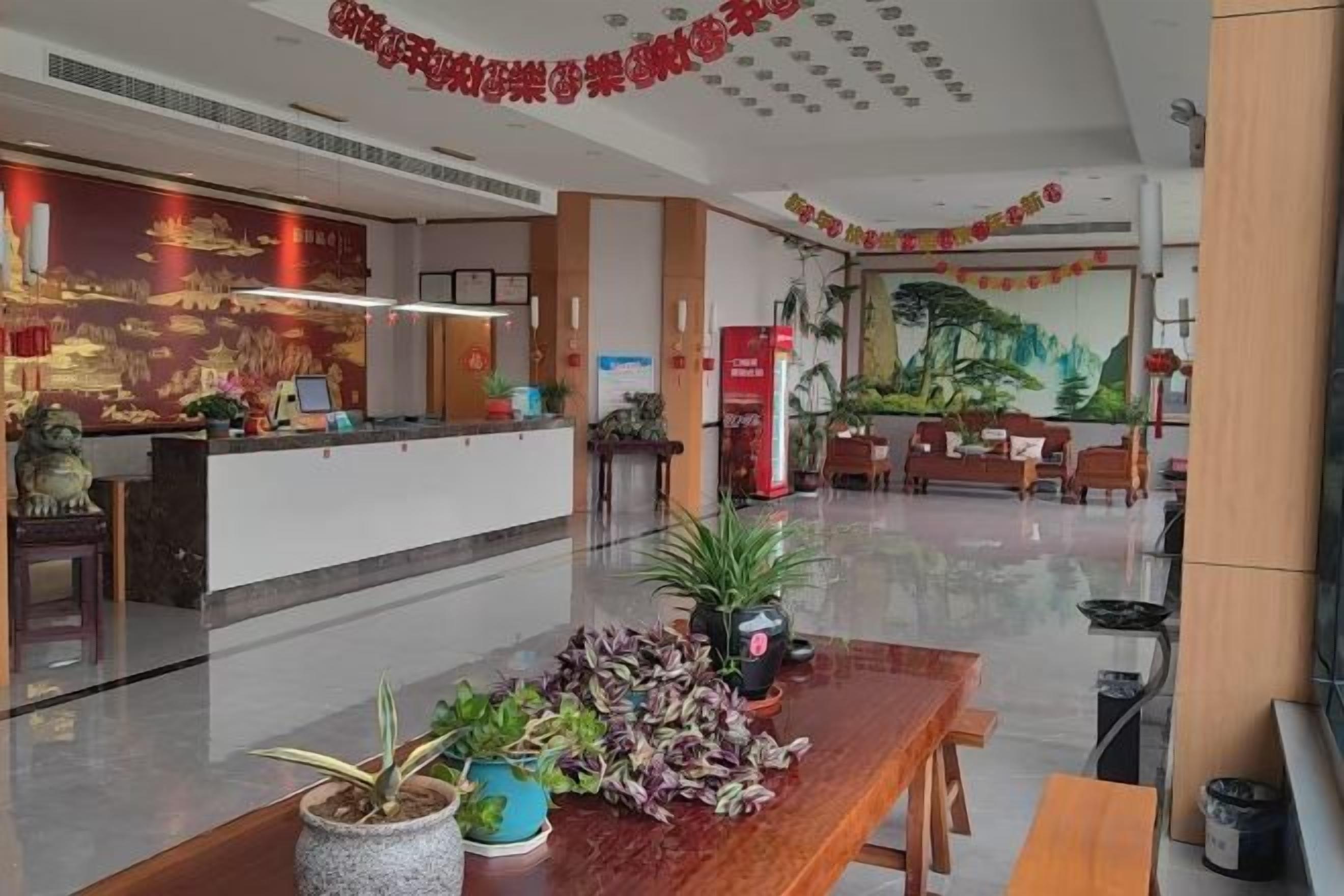 A hotel reception area with a reception desk, seating area, and decorative plants.