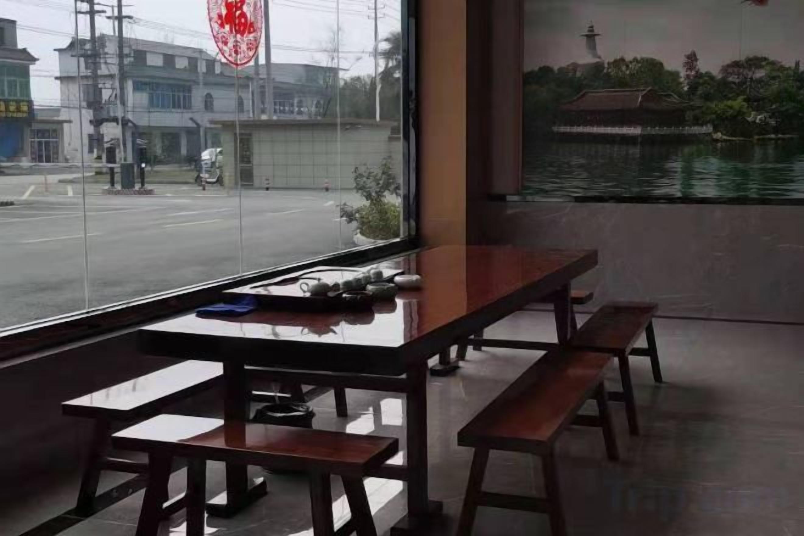 A restaurant with a view of a street and a body of water. There are wooden tables and benches.