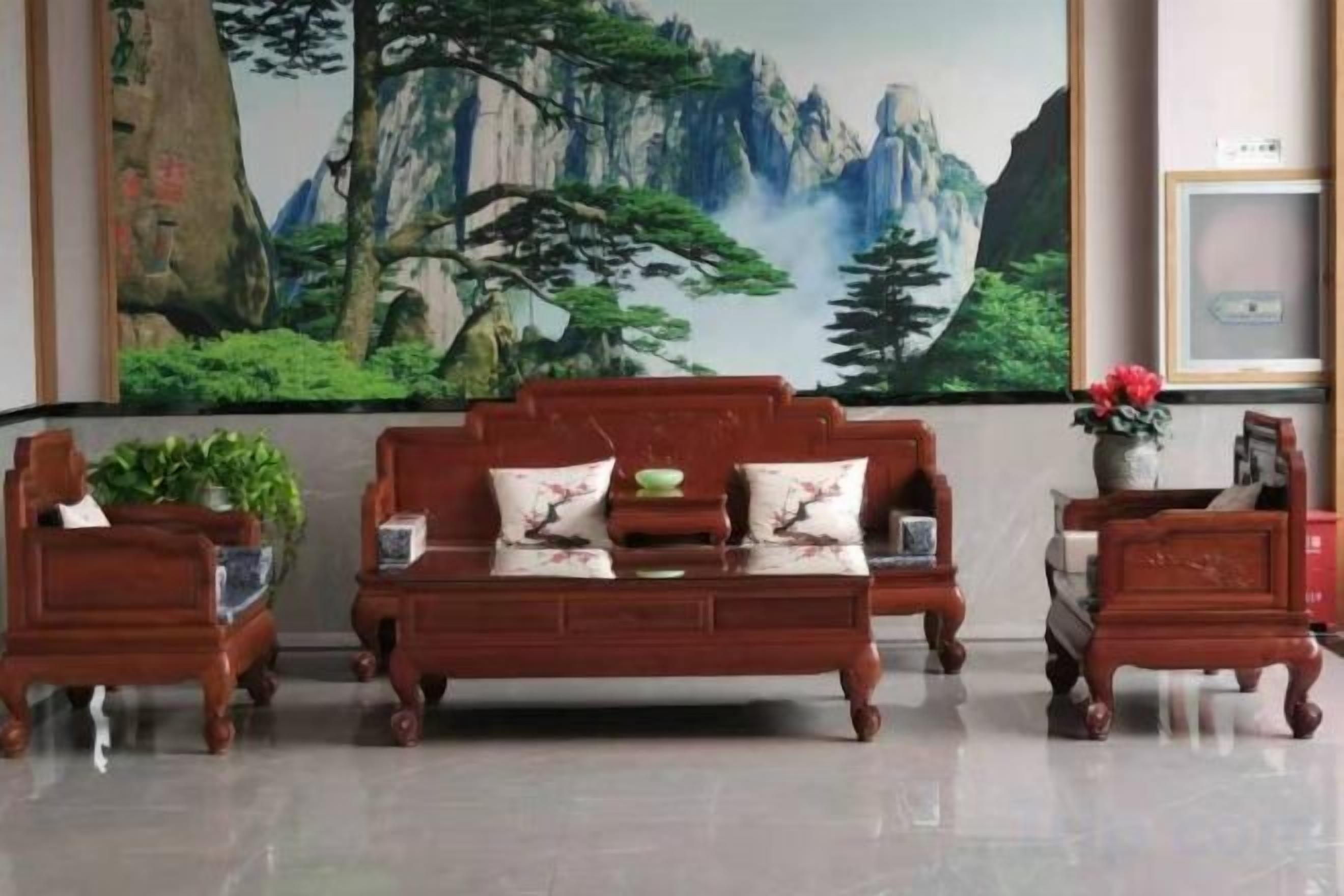 A traditional wooden sofa set with a matching armchair and side table, positioned in front of a large landscape painting.